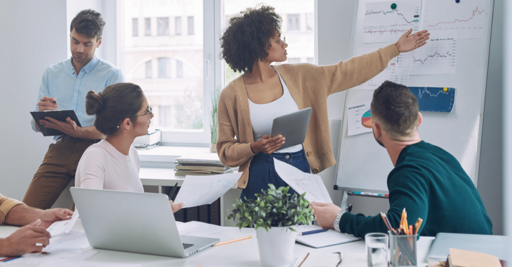 Women and men in a boardroom looking at a whiteboard